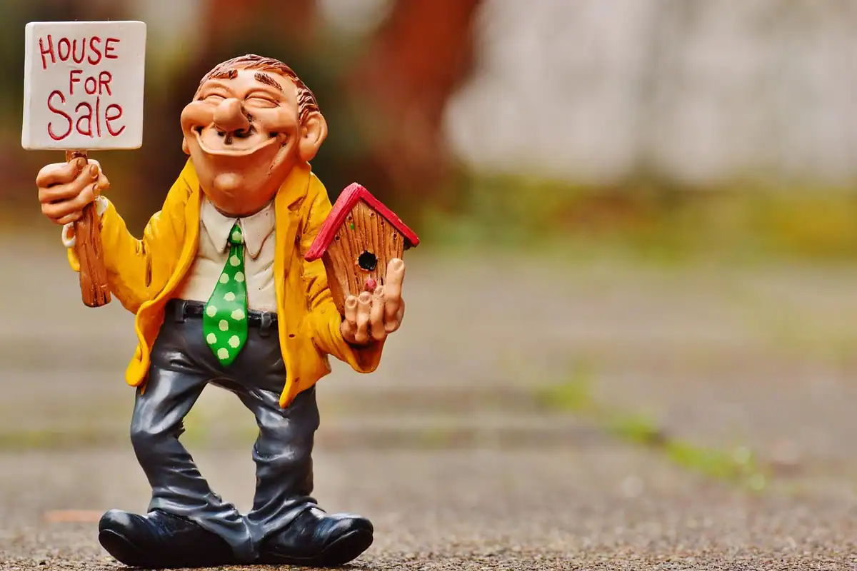 Figurină de agent imobiliar în costum lângă o căsuță în miniatură, simbol al vânzării unei locuințe