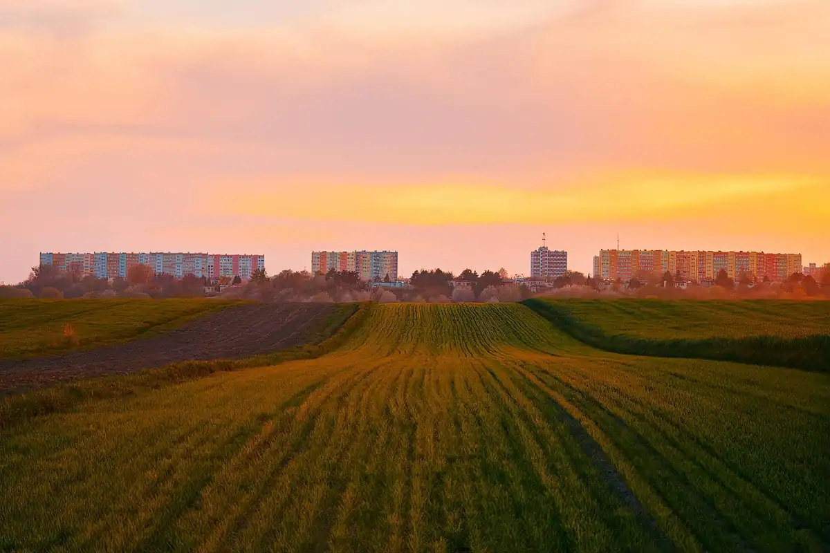 Peisaj urban la apus, cu blocuri de apartamente la marginea orașului și câmpuri în fața lor