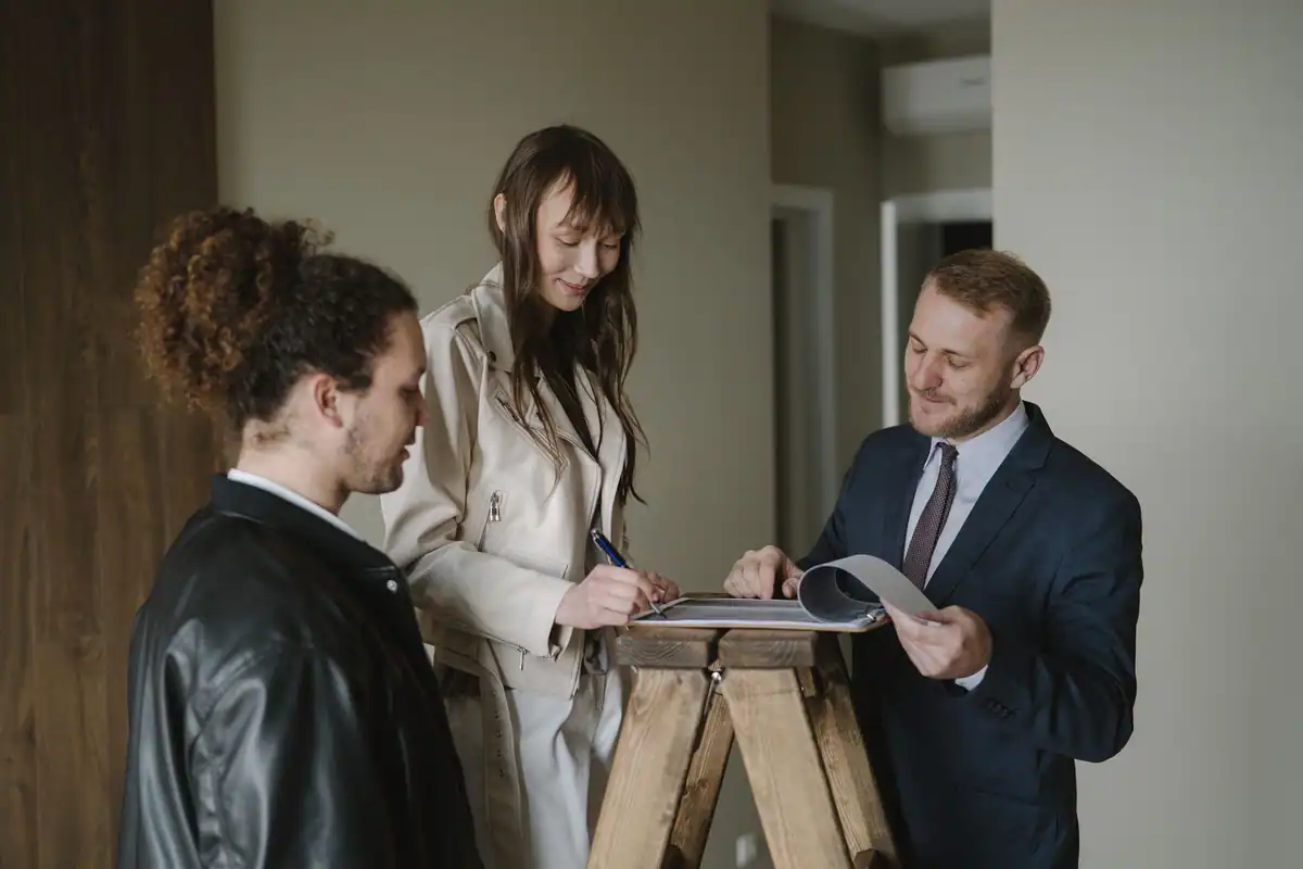 Cuplu care semnează documente imobiliare împreună cu un agent, într-un apartament nou