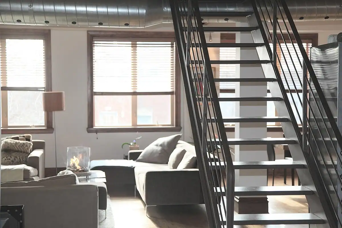 Apartament tip loft cu scară metalică, canapea gri și ferestre înalte