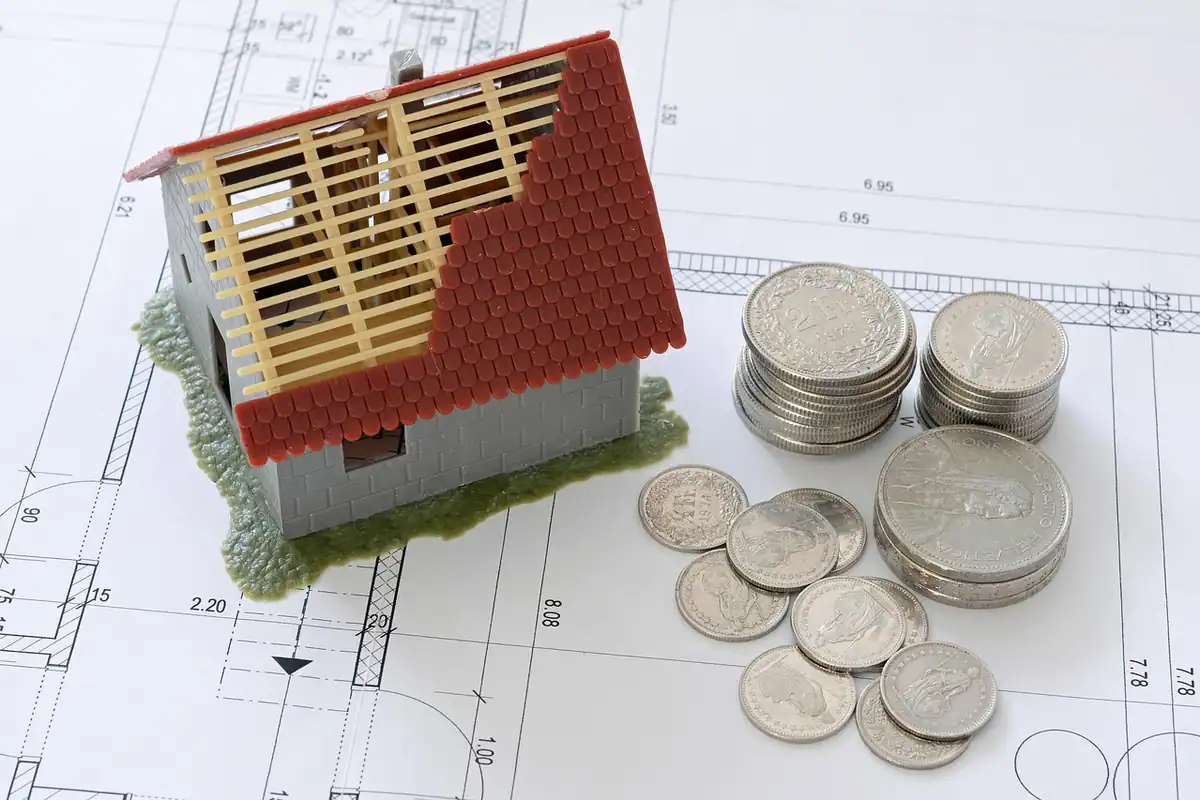 Casă în construcție lângă monede, deasupra unui plan desenat