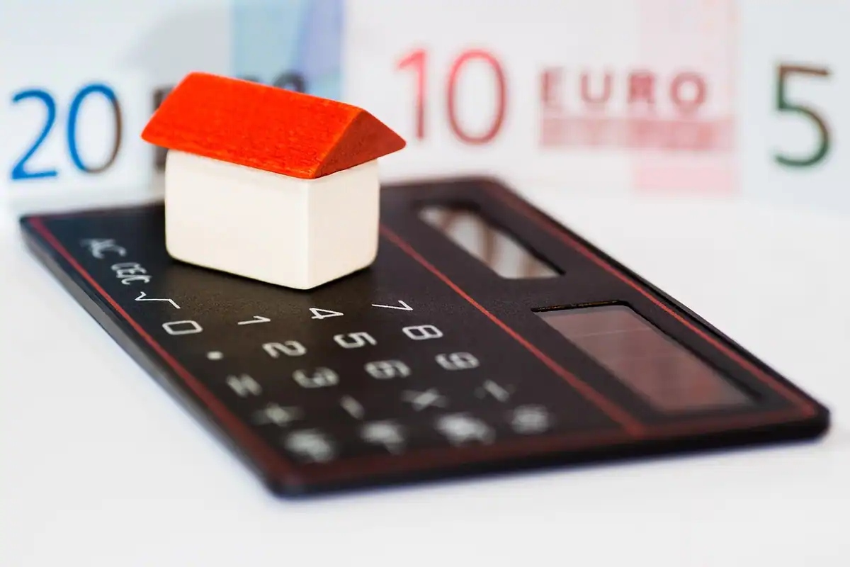 Casă, bancnote în euro și un calculator pe masă, pentru calculul unui credit imobiliar
