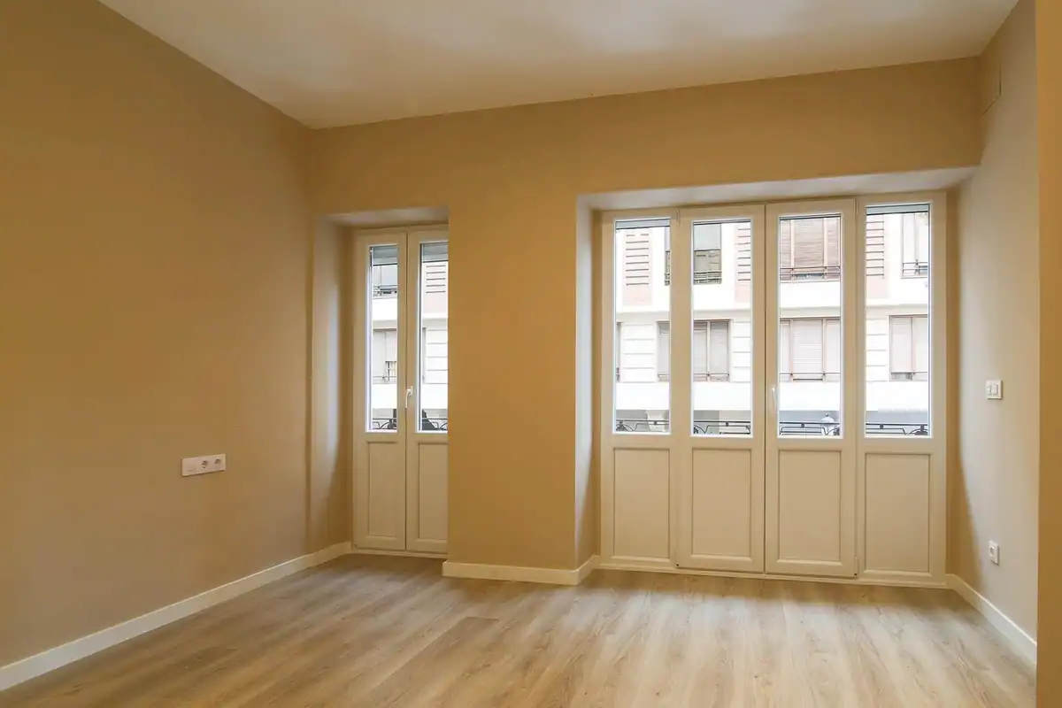 Cameră goală cu pereți bej, parchet și uși-balcon, pregătită de renovare