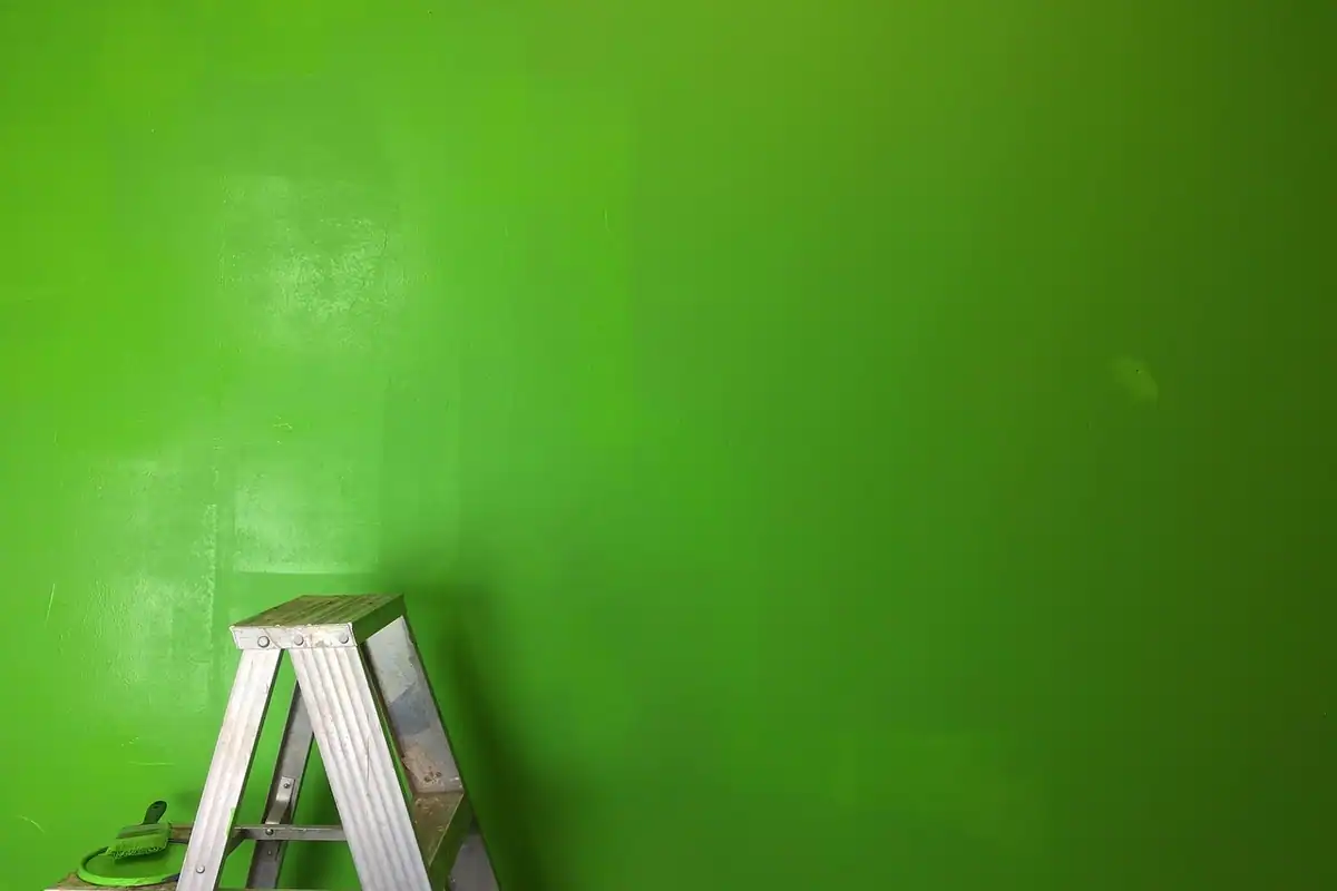 Scară verde lângă un perete proaspăt zugrăvit, cu pensule de vopsea, într-o cameră în renovare