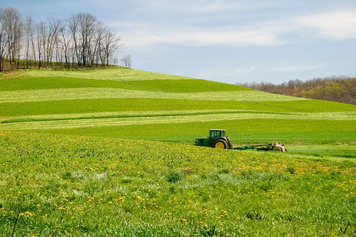 Tractor pe un câmp verde cu dealuri line și copaci în depărtare